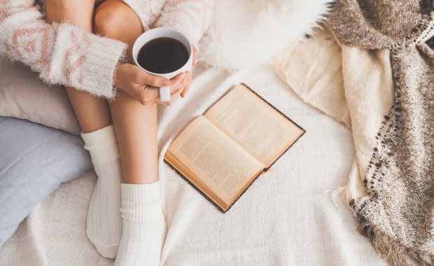 Девушка пьет кофе и читает книгу.