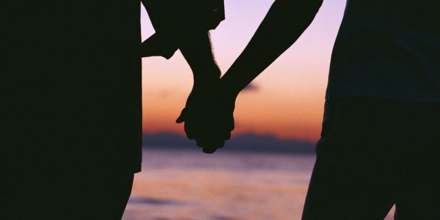 Пара на пляже держатся за руки.
